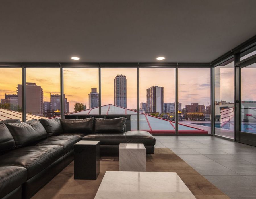 Optima Lakeview® Apartments in Chicago, IL Modern living room with black sofa, large windows, city skyline, and sunset in the background.