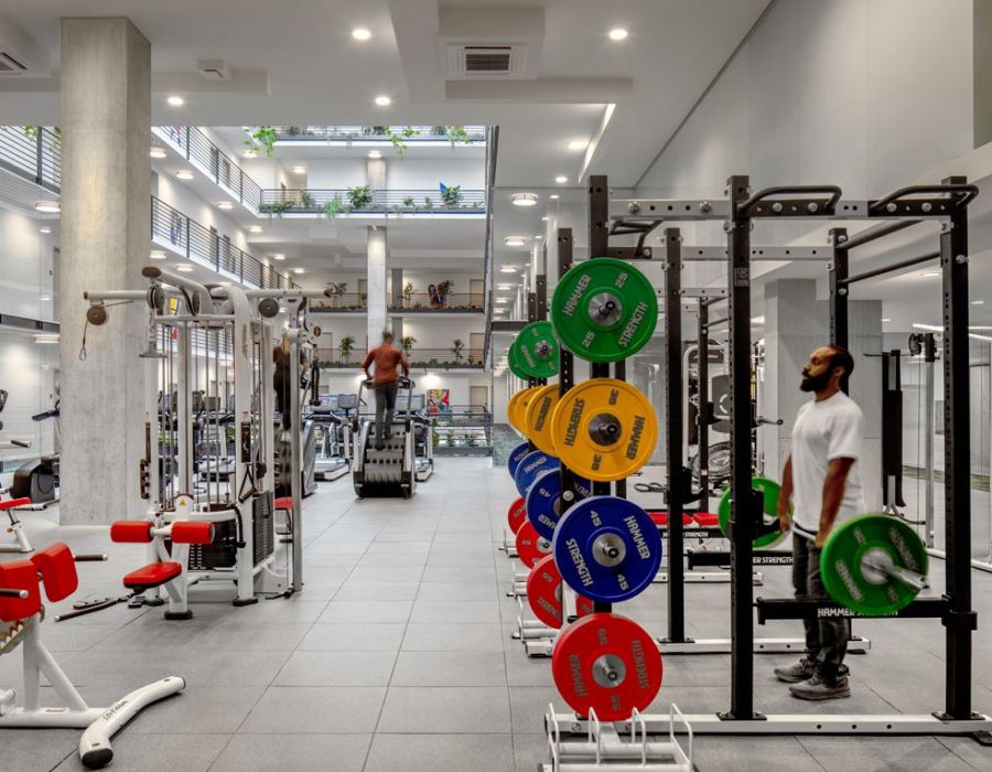 Optima Lakeview® Apartments in Chicago, IL Modern gym with weightlifting equipment, colorful weights, and people exercising in a bright, spacious room.