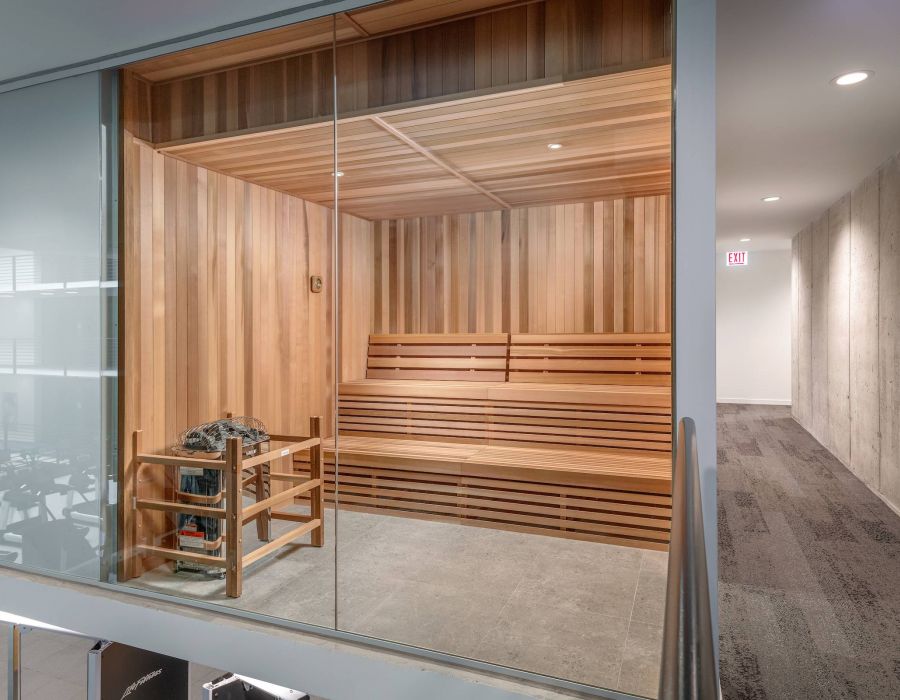 Optima Lakeview® Apartments in Chicago, IL Modern wooden sauna with glass wall, benches, and heater, next to a hallway with gray carpet.